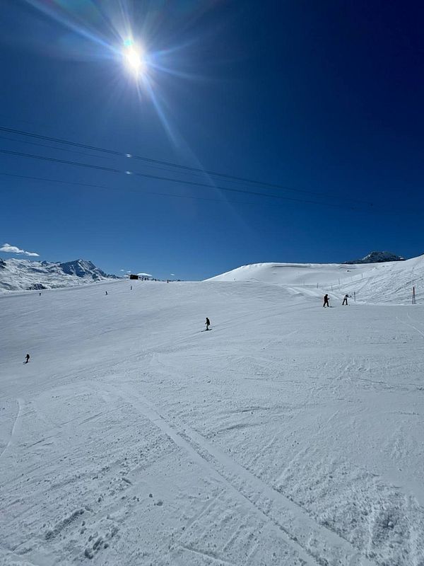 A bright, sunny day on a ski slope with several skiers enjoying the snow.