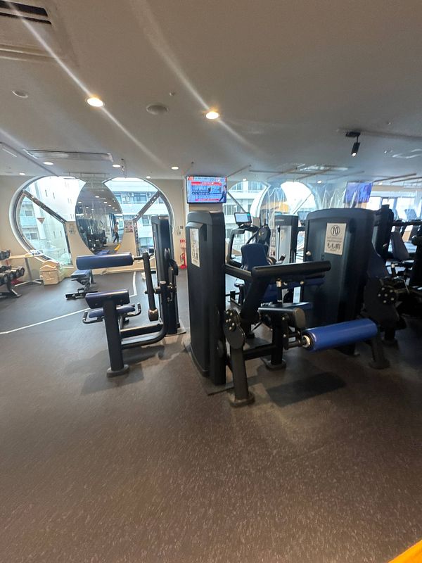 A gym interior featuring various exercise machines and large windows.