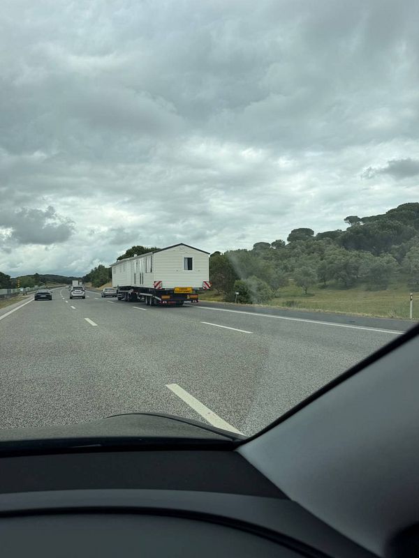 A small wooden house built on a trailer is being driven on a highway in Portugal.