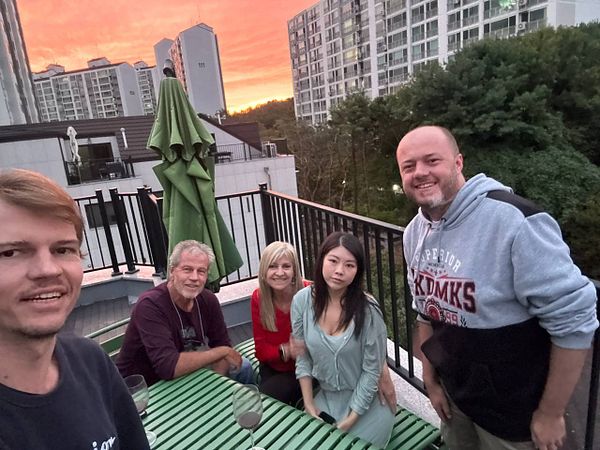 A group of five people gathered on a rooftop terrace during sunset in a Korean residential area.
