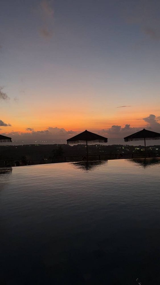 A serene sunset view over a pool with umbrellas in the foreground.