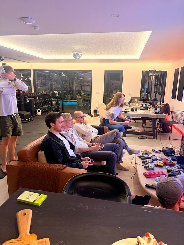 A group of people gathered in a cozy living room playing video games and working at desks in a modern home space.