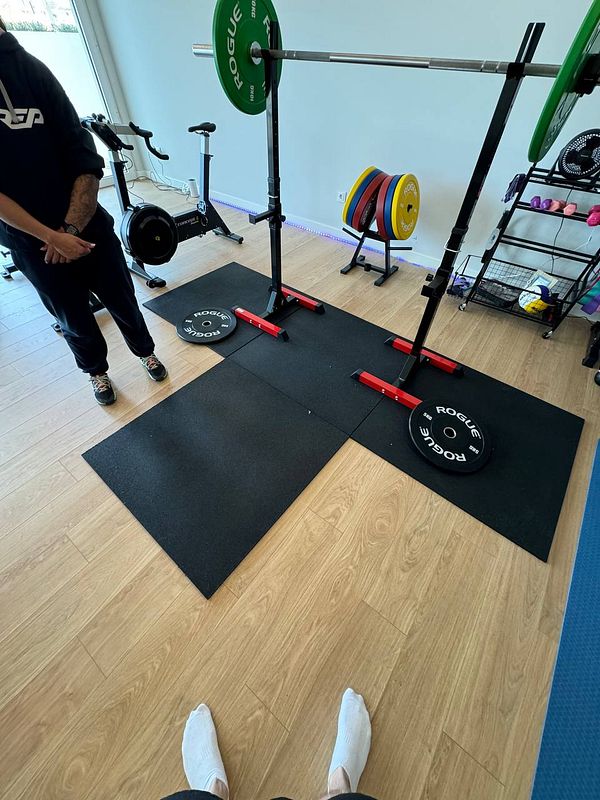 A home gym setup featuring weightlifting equipment and a personal trainer.