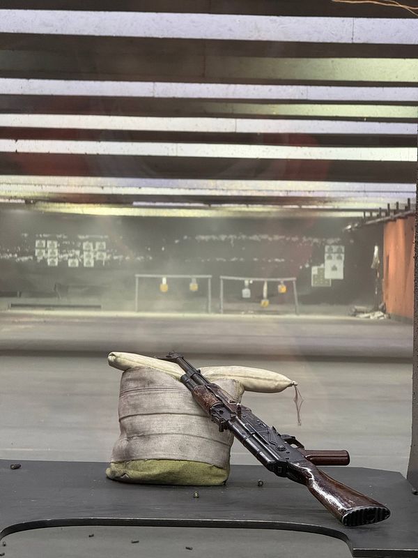 Photograph of an outdoor shooting range with several shooters positioned along lanes, brick target stands, and a gravel path.
