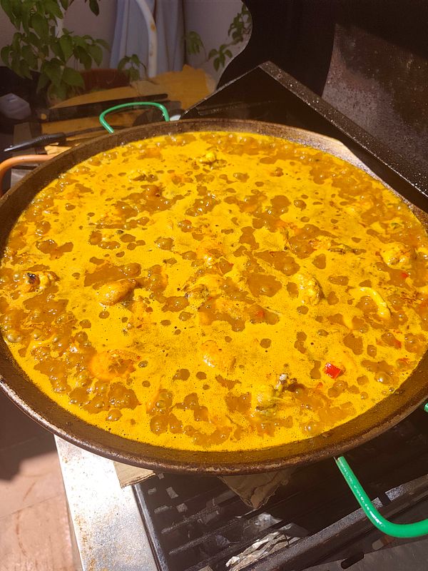 A serene beach scene at sunrise with breakfast including homemade paella served outdoors on a wooden table near the shore.