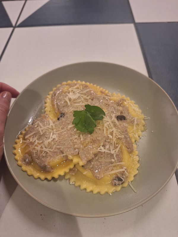 A plate of three-cheese truffle ravioli topped with a creamy brown butter sage sauce and garnished with parsley.