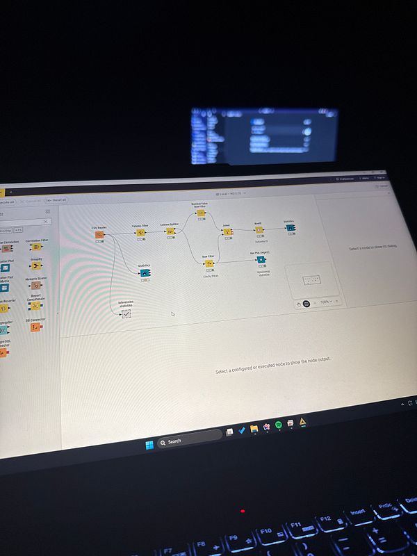 A laptop screen displays a data analysis workflow in KNIME, with a dark background and a secondary screen visible in the background.