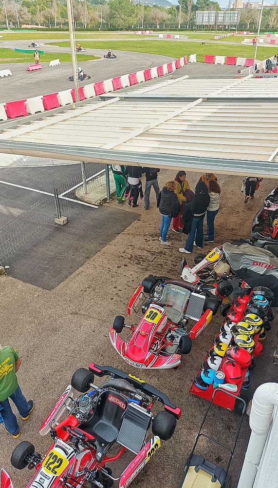 The image captures a kart racing venue with karts, helmets, and a group of people preparing for racing.