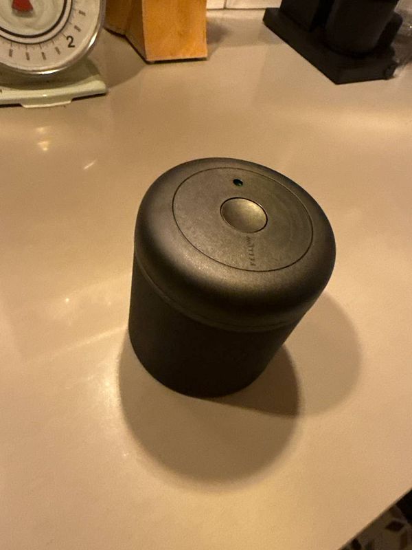 A black Fellow can is placed on a countertop next to a vintage kitchen timer.