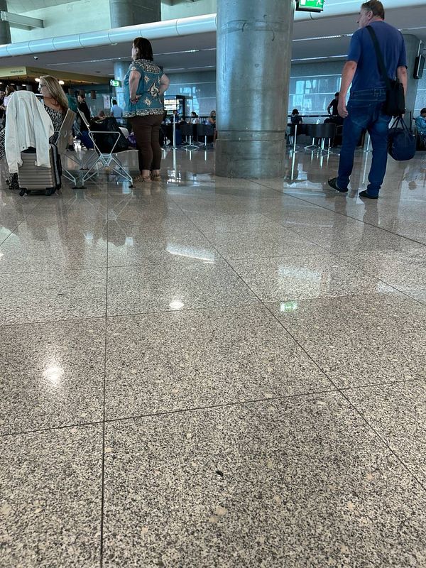 The image captures a busy airport terminal scene with travelers waiting and moving about.
