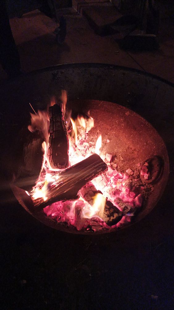 A glowing fire in a circular pit, surrounded by glowing embers and logs.