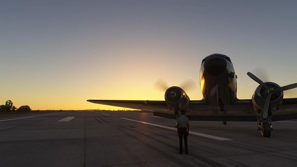 A vintage aircraft is positioned on a runway at sunset, with a person standing in front of it.