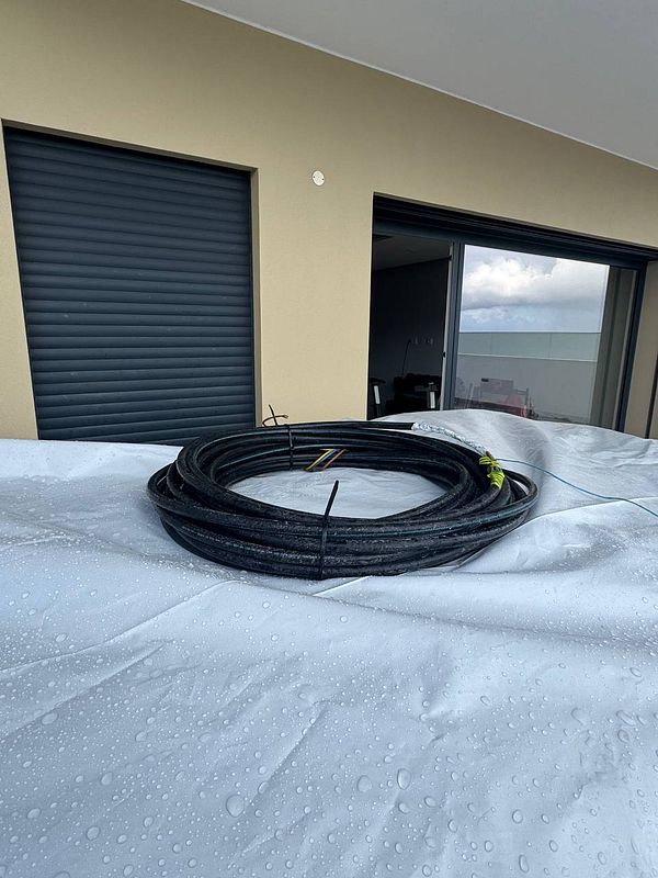 A close-up view of a wet tarp covering sauna wood in a garden, with a coiled black hose on top.