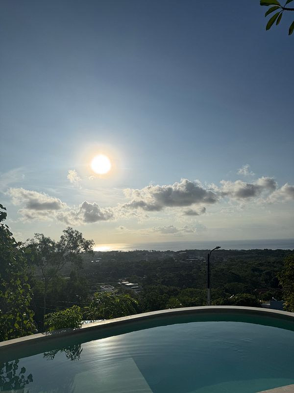 A scenic view of a sunset over a lush landscape with a pool in the foreground.