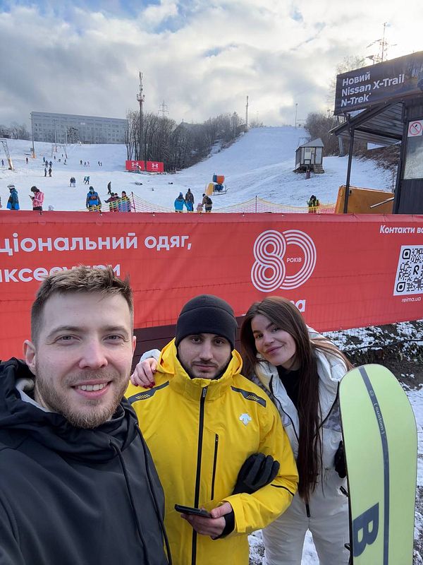 A group of three friends poses for a selfie on a snowy ski slope.