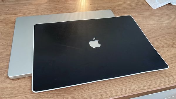 A MacBook with a black leather skin is placed on top of a silver MacBook on a wooden surface.