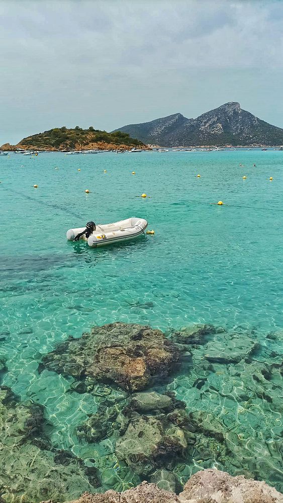 A serene beach scene featuring a small boat anchored in clear turquoise waters with rocky formations visible beneath the surface.
