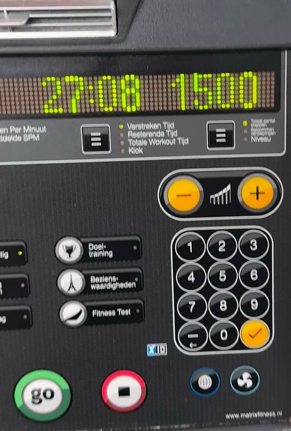 A digital photograph of a Stairmaster fitness machine in a gym setting with gym equipment and people in the background.