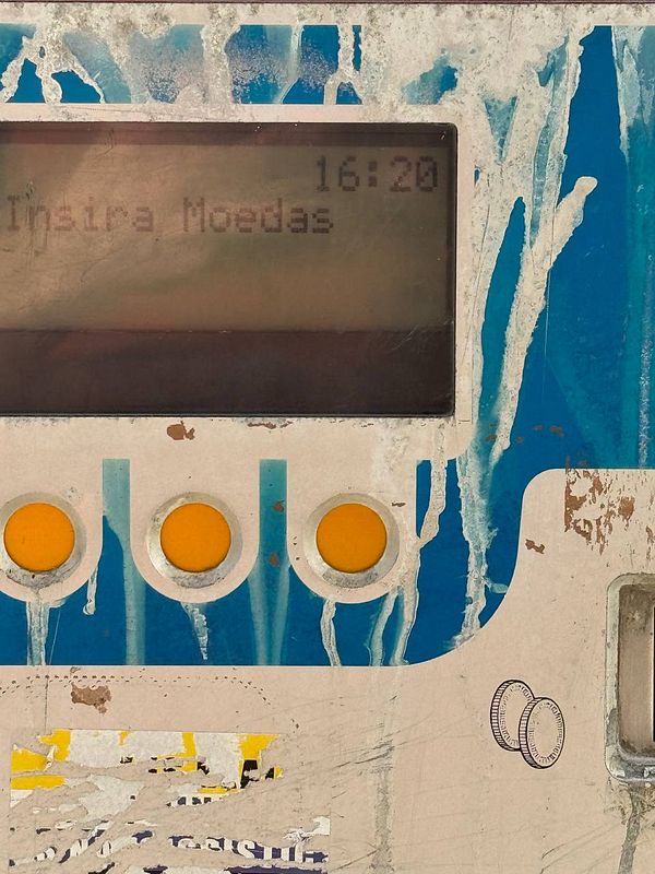 A close-up view of a weathered parking meter in Lisbon displaying a message about coin payment.