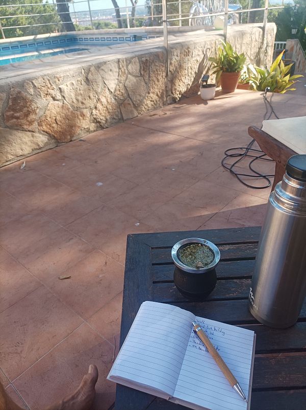 A serene outdoor workspace featuring a notebook, a mate cup, and a thermos.