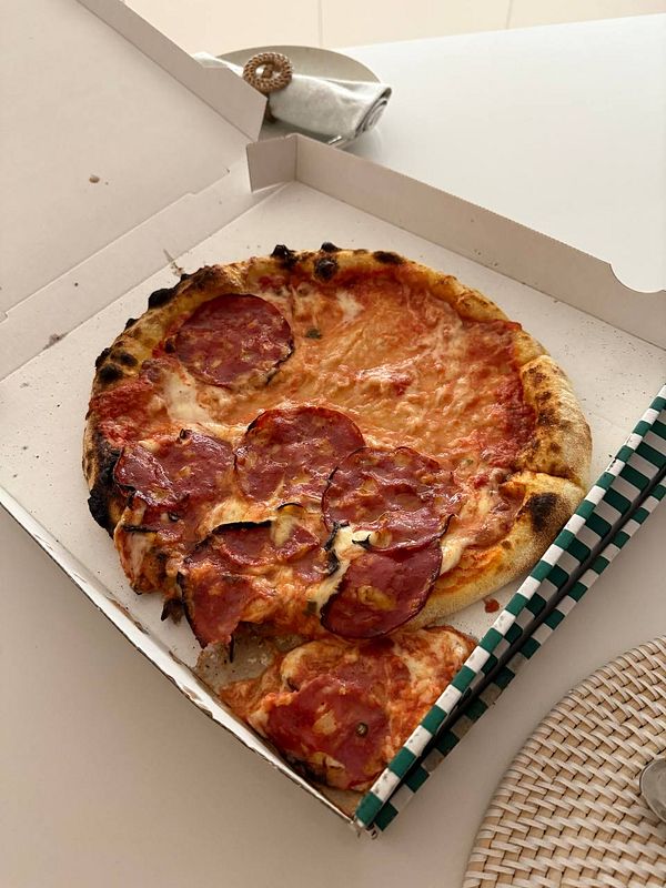 A pizza with pepperoni is displayed in an open pizza box on a table.