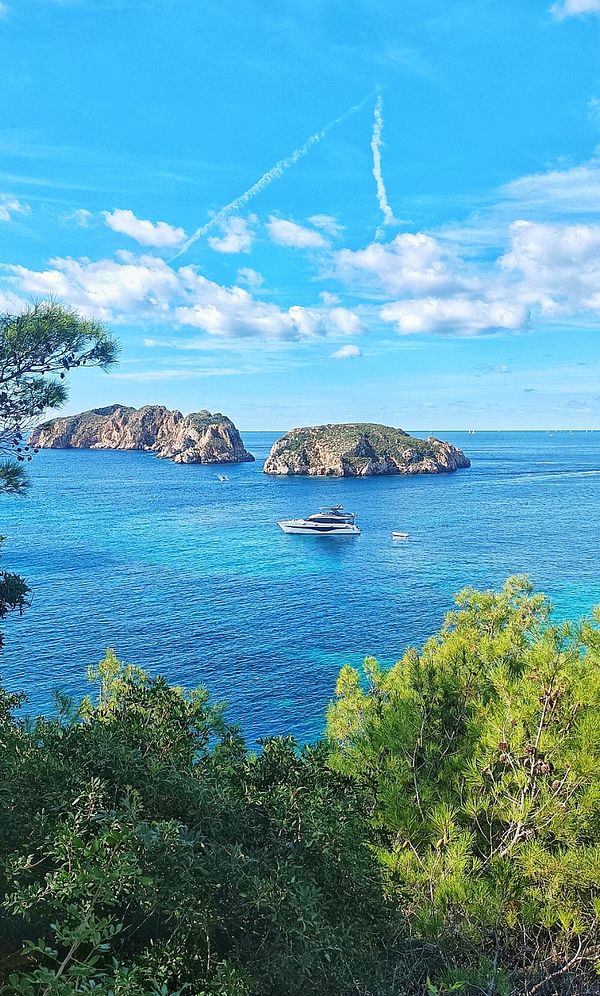 A scenic view of a tranquil sea with two islands and a yacht.