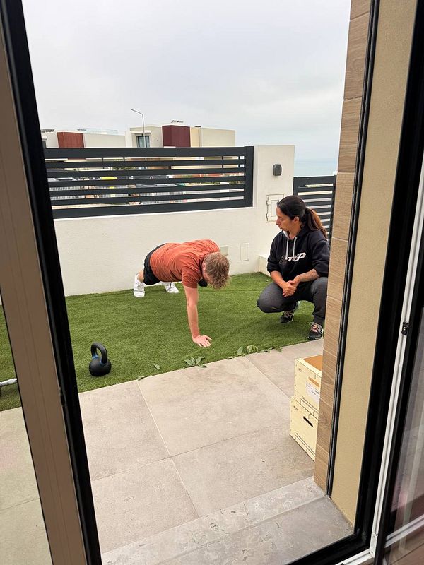A man performs push-ups on a grassy area while a woman observes and provides guidance.
