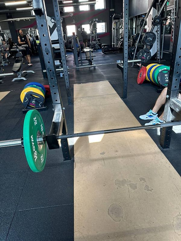 A gym scene featuring a barbell with weight plates and workout equipment in the background.