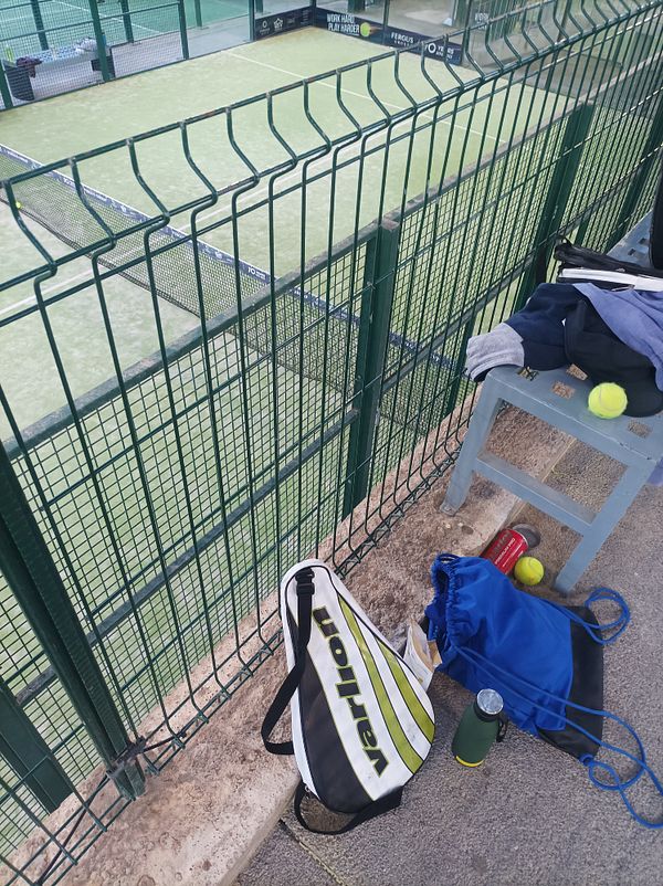 A view of a padel court with personal items and equipment nearby.