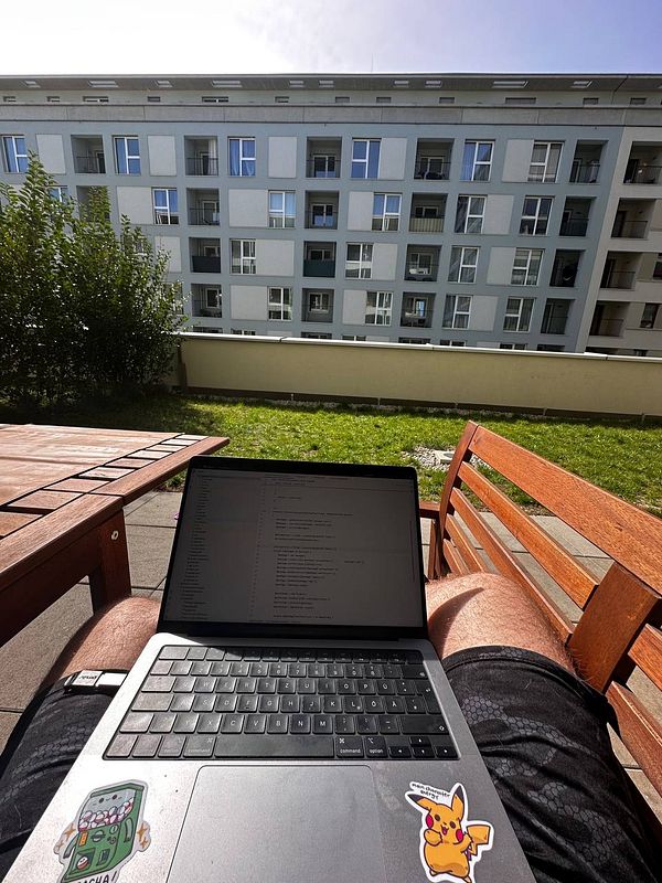 A person is working on a laptop outdoors in their garden, enjoying the sunshine after a long time.