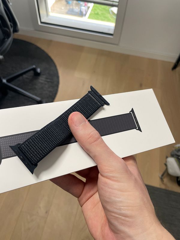 A hand holds a black sport Apple Watch bracelet above its packaging.