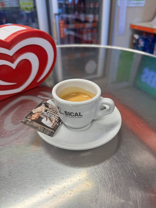 A small cup of espresso is placed on a shiny metal table next to a packet of sugar.