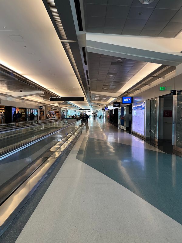 A spacious airport terminal corridor with shops and travelers.