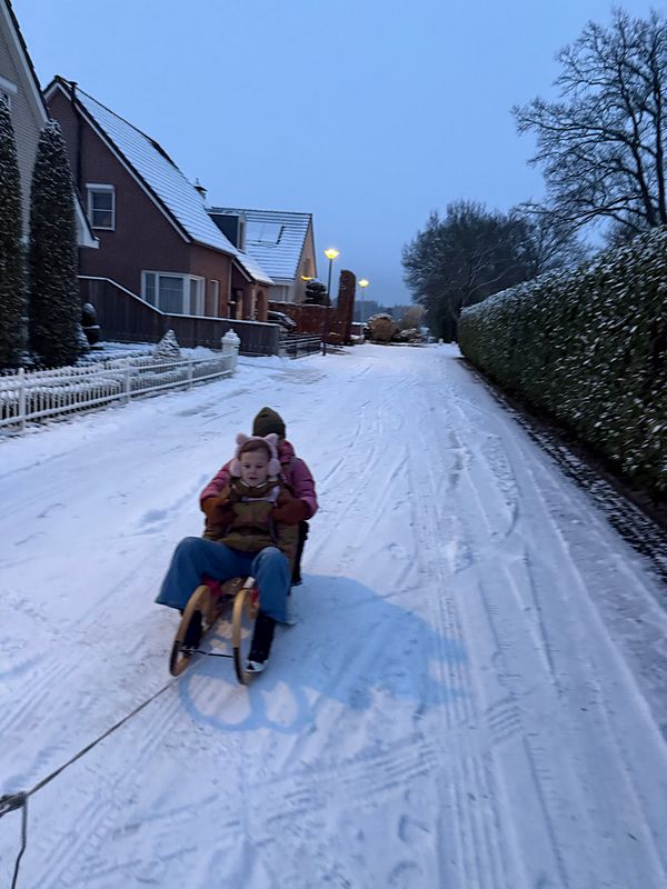 A child sledding on a snowy slope with a backpack in a winter forest setting during daytime.