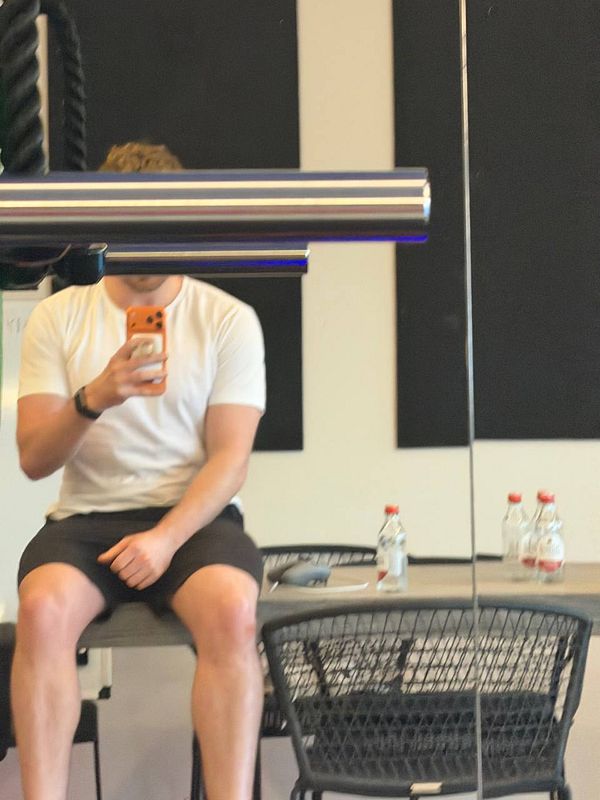 A person is sitting on a table in a gym-like environment, taking a selfie.