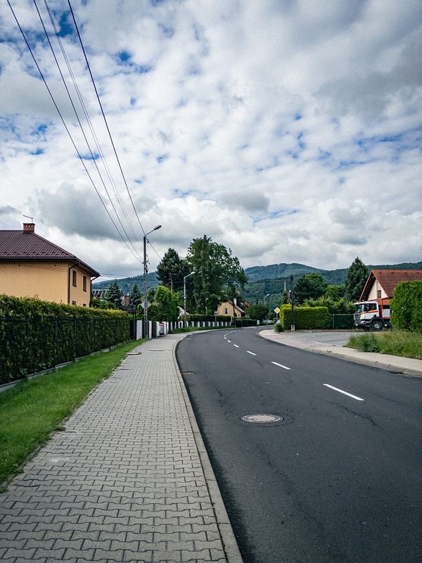 A peaceful urban street view in the early morning with residential and commercial buildings under a blue sky with scattered clouds.