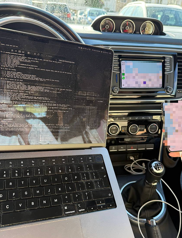 A laptop with code and instructions open, placed inside a 2018 VW Beetle car, showing the car's dashboard with a touchscreen displaying a mobile interface and a manual gear stick.
