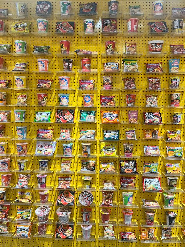 A vibrant display of various instant noodle products arranged on a bright yellow wall.