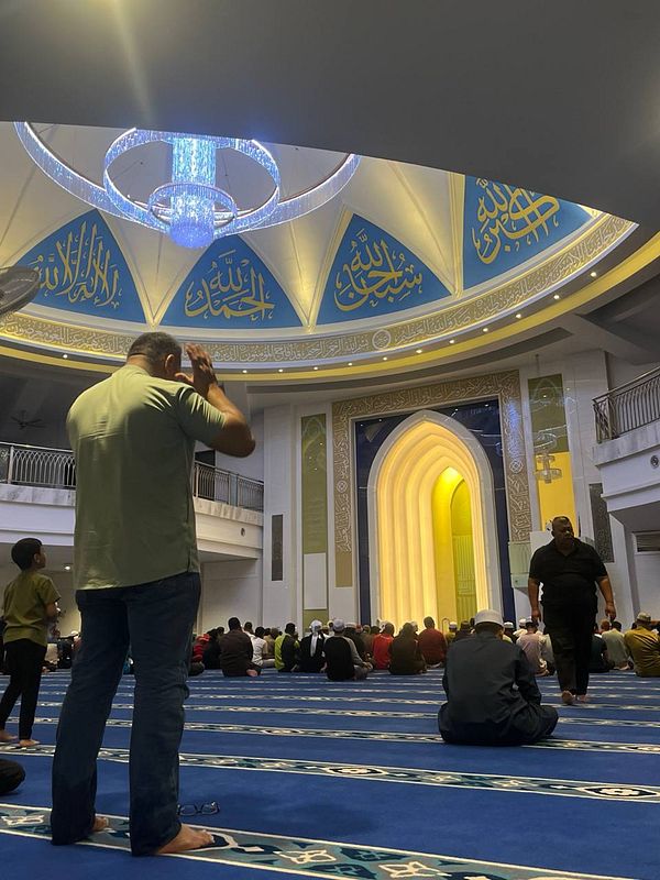 A group of worshippers is gathered inside a mosque, engaged in prayer.