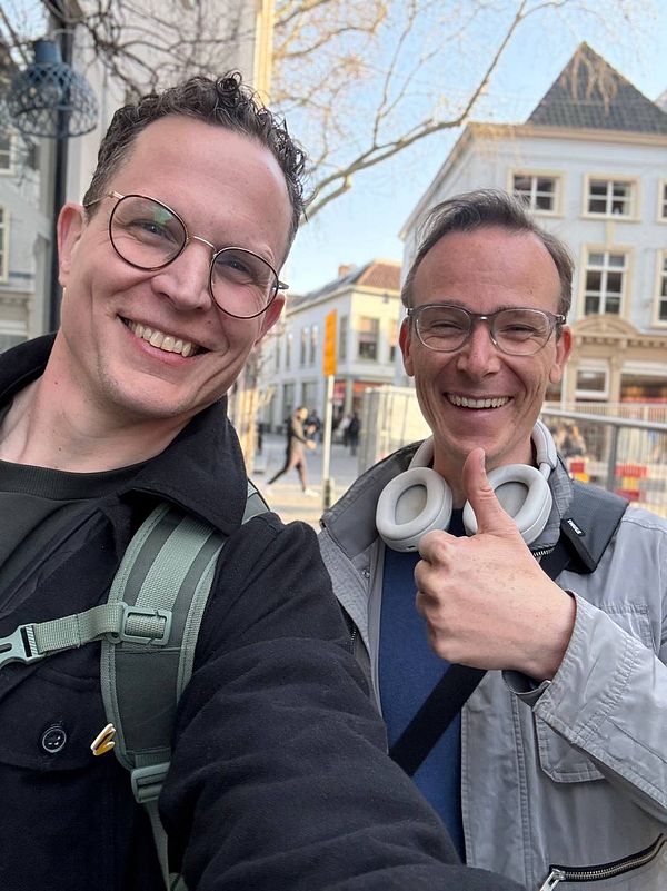 Portrait of a man standing in front of greenery wearing a dark jacket and white shirt.