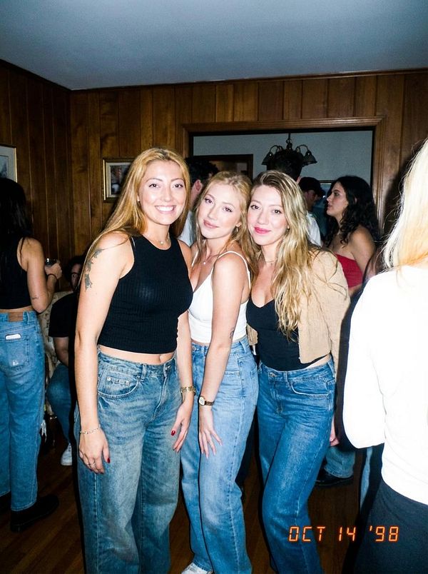 Three women pose together in a lively indoor setting, showcasing a retro vibe.