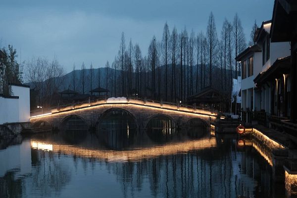 Scenic lakeside view of Xianghu Hu with a pavilion, willow trees, and a calm water reflection under a cloudy sky.