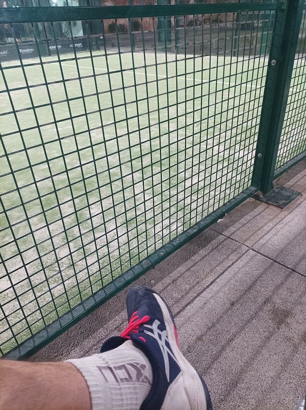 A close-up view of a foot resting on a bench near a padel court.
