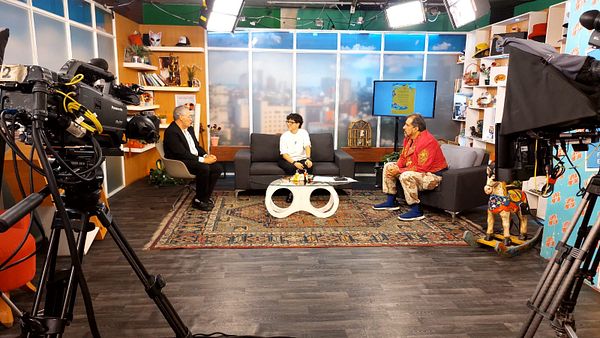 A TV interview set featuring three individuals discussing a book.