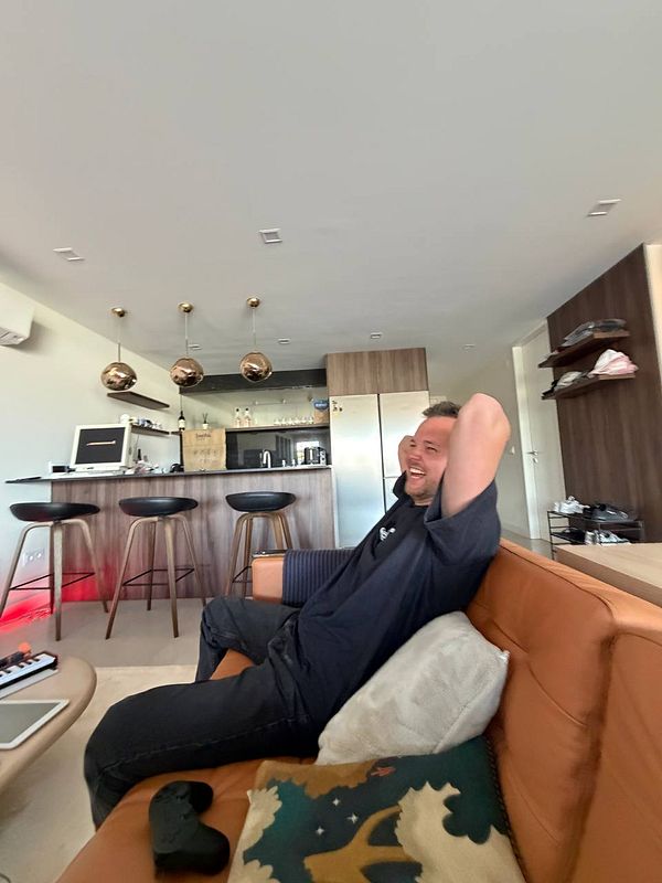Man sitting on a couch working on a laptop with a tablet and phone on the side table in a cozy living room setting.