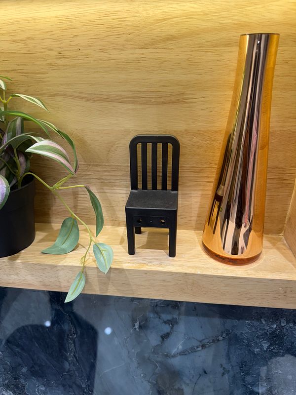 A decorative shelf displays a small black chair, a plant, and a shiny copper vase.