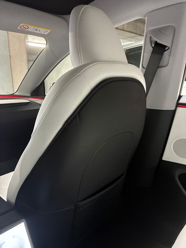 Front seat back covers installed on a Tesla car interior, featuring smooth leather-like texture and black color.