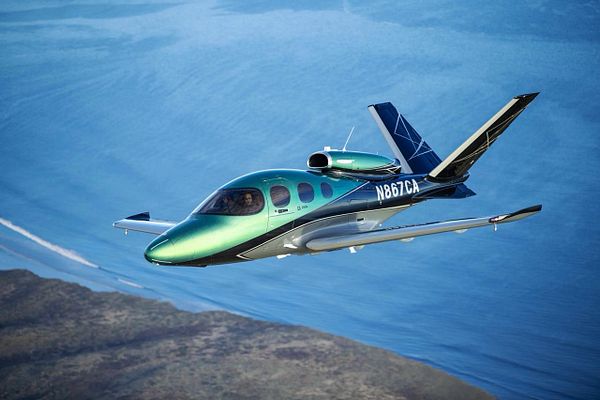 Top-down view of a Cirrus Vision Jet SF50 aircraft on a runway surrounded by green fields and buildings.