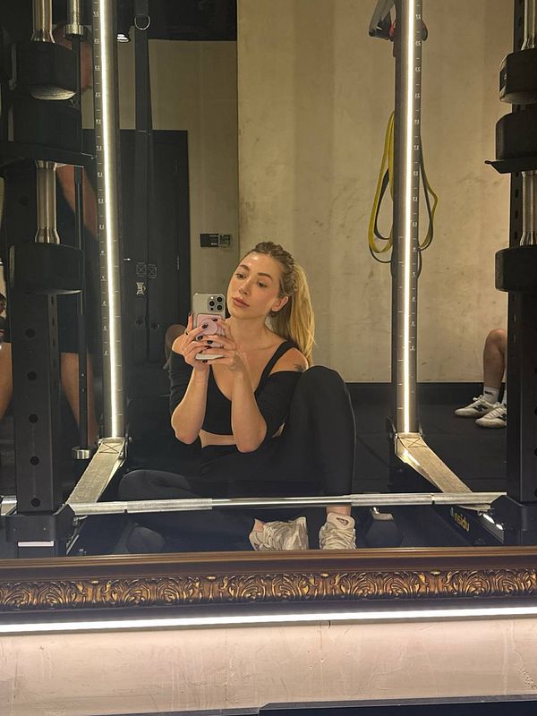 A woman is taking a selfie in a gym setting, showcasing her workout attire and the gym's equipment.