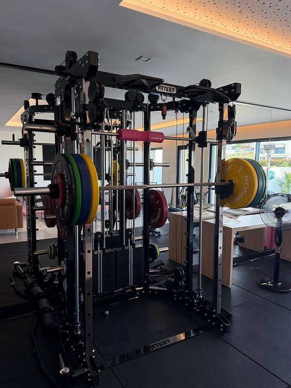 A person performing a heavy squat in a gym with a weightlifting belt and knee sleeves, spotted by a personal trainer.